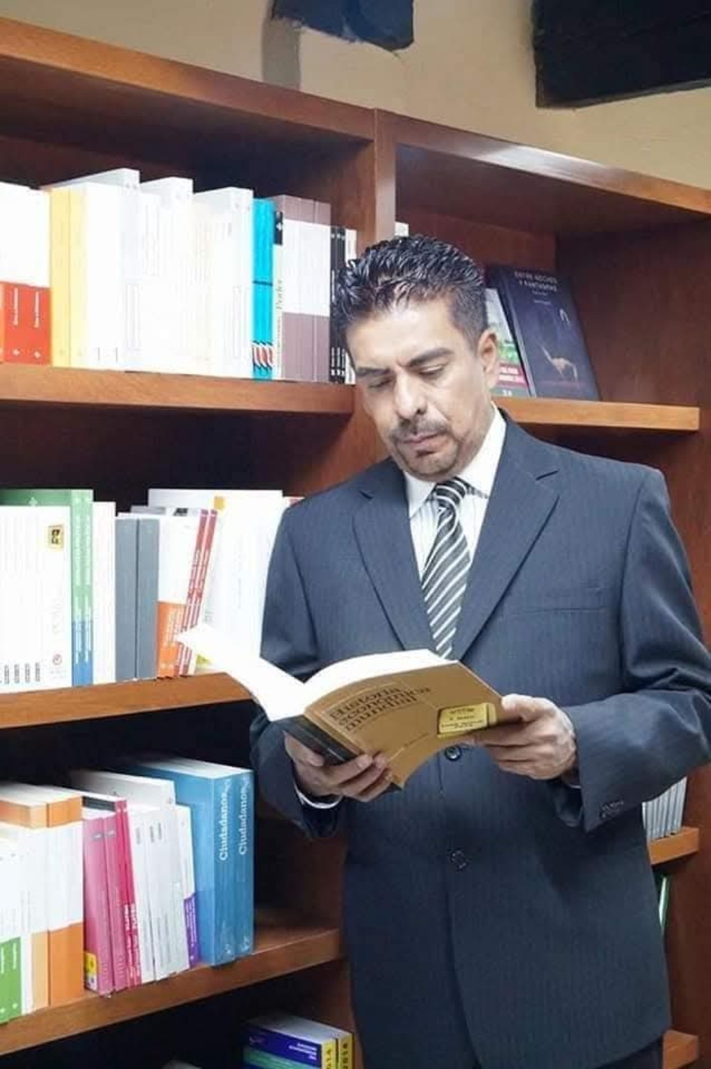 José Cruz Medina Rodríguez leyendo un libro frente a una biblioteca